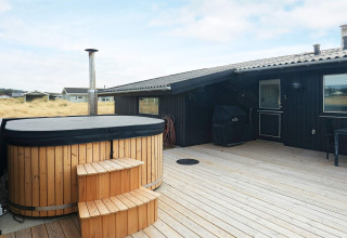 Wooden terrace with a hot tub and barbecue at the 7-person holiday home in Hjørring, Denmark.