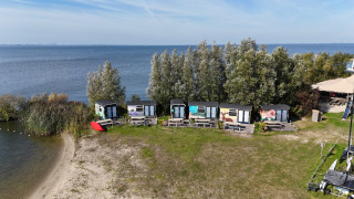Luftaufnahme von Tiny Wagon Lodge mit kleinen bunten Hütten am Ufer und Bäumen im Hintergrund.