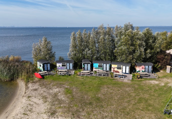 Luftaufnahme von Tiny Wagon Lodge mit kleinen bunten Hütten am Ufer und Bäumen im Hintergrund.