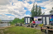 Twee mensen aan tafel bij kleurrijke tiny wagons aan Marina Parcs Almere, Nederland, vlak bij het water.
