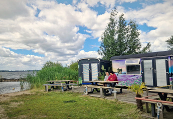 Due persone sedute davanti a tiny wagons colorate al Marina Parcs Almere, Paesi Bassi, vicino al lago.