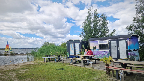 Due persone sedute davanti a tiny wagons colorate al Marina Parcs Almere, Paesi Bassi, vicino al lago.