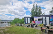 Zwei Personen sitzen vor bunten Tiny Wagons an der Marina Parcs Almere in den Niederlanden am Wasser.