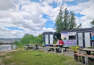 Zwei Personen sitzen vor bunten Tiny Wagons an der Marina Parcs Almere in den Niederlanden am Wasser.