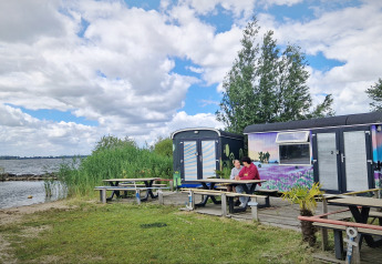 Dos personas sentadas junto a coloridas tiny wagons en Marina Parcs Almere, Países Bajos, cerca del lago.