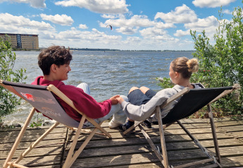 Due persone si rilassano su sedie sdraio vicino all’acqua al Tiny Wagon a Marina Parcs Almere, Paesi Bassi.