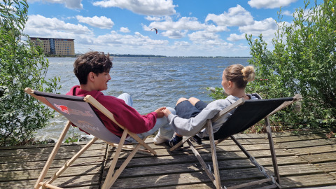 Zwei Personen entspannen sich in Liegestühlen am Wasser bei Tiny Wagon im Marina Parcs Almere, Niederlande.