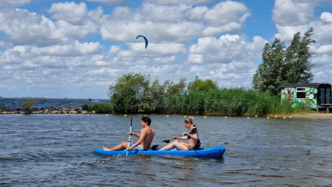 Un couple pagaie en kayak bleu devant une tiny wagon à Marina Parcs Almere, Pays-Bas.