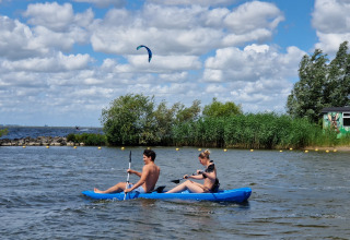 To personer padler i en blå kajak foran en grøn vogn ved Tiny wagon, Marina Parcs Almere, Holland.