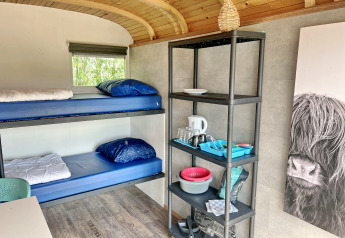 Interno del Tiny wagon lodge a Marina Parcs Almere, Paesi Bassi, con letti a castello e scaffale cucina.