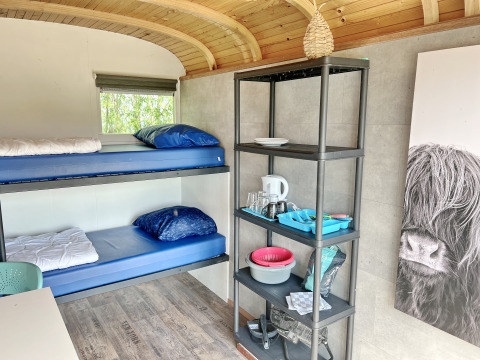 Interiør af Tiny wagon lodge i Marina Parcs Almere, Holland, med køjesenge og hylde med køkkenudstyr.