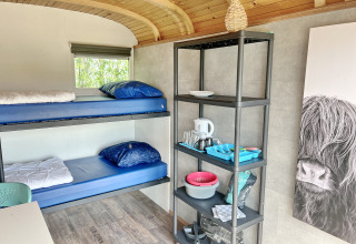 Interno del Tiny wagon lodge a Marina Parcs Almere, Paesi Bassi, con letti a castello e scaffale cucina.