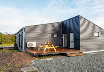 Modern 8-person holiday lodge in Ansager with black wood siding, deck, picnic table, and outdoor seating.