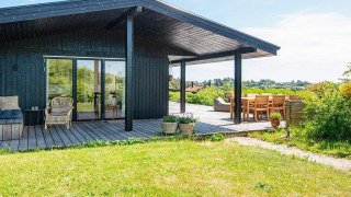 Sunny deck with seating area at 8 person holiday home in Ebeltoft, surrounded by greenery and open views.