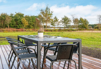 Outdoor dining table with six chairs on wooden deck overlooking green field at 8 person holiday home in Ansager.