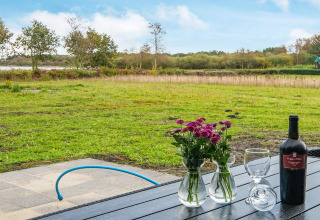 Vista dal lodge con vino, fiori e bicchieri sul tavolo, campo verde ad Ansager, Danimarca.