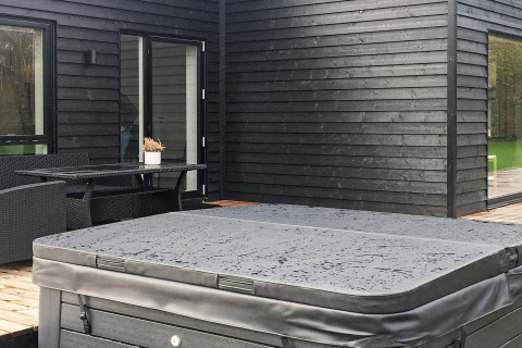 Buitenruimte van vakantiehuis in Ansager, Denemarken, met overdekte jacuzzi en zwarte houten gevel.
