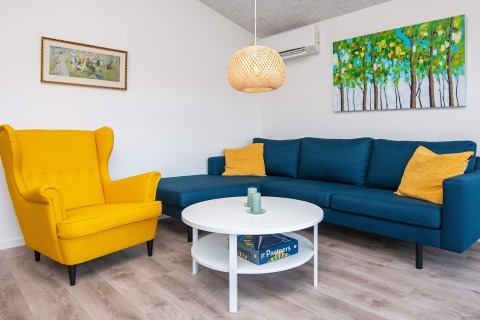 Wohnzimmer eines Ferienhauses in Ansager, Dänemark mit gelbem Sessel, blauer Couch und moderner Deko.
