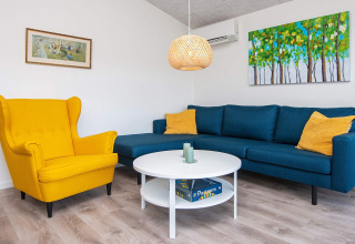 Woonkamer van vakantiehuis in Ansager, Denemarken met gele stoel, blauwe bank en moderne schilderijen.