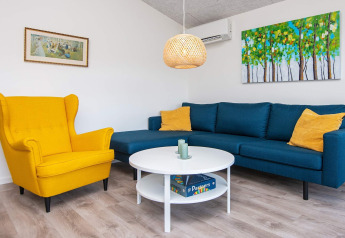 Sala de casa vacacional en Ansager, Dinamarca, con sillón amarillo, sofá azul y arte en las paredes.