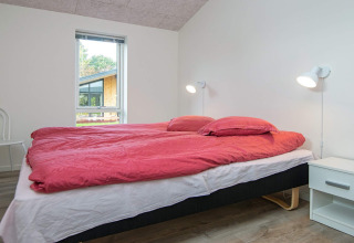 Slaapkamer met tweepersoonsbed, rood beddengoed, nachtkastjes en wandlampen in vakantiehuis Ansager, Denemarken.