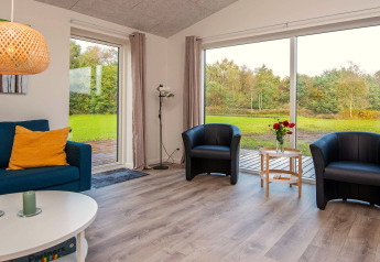Salon lumineux dans une maison de vacances à Ansager, Danemark, avec grandes baies vitrées et vue sur la nature.