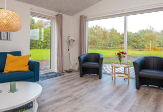 Helles Wohnzimmer in einem Ferienhaus in Ansager, Dänemark, mit großen Fenstern und Blick ins Grüne.