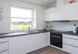 Moderne weiße Küche mit großem Fenster und Geräten im 8-Personen-Ferienhaus in Ansager, Dänemark.