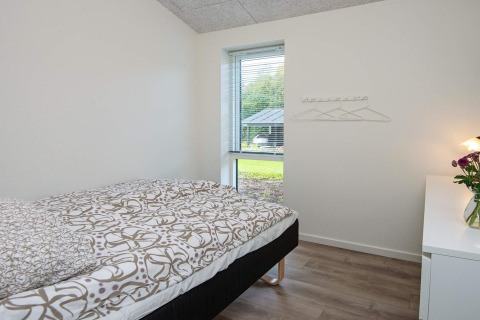 Lichte, eenvoudige slaapkamer met eenpersoonsbed en uitzicht op tuin in een vakantiehuis in Ansager, Denemarken.