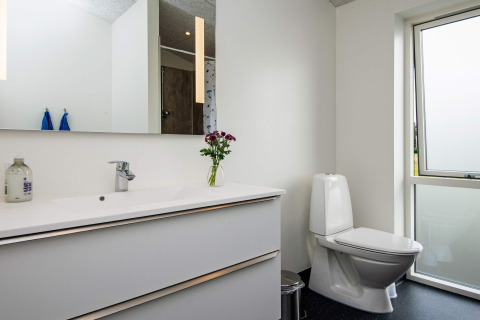 Modernes Badezimmer mit weißem Waschbecken, Spiegel, Toilette und Fenster im Ferienhaus in Ansager, Dänemark.