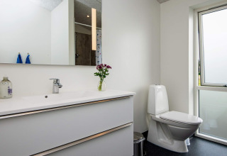Modern badkamer met wit wastafelmeubel, groot spiegel, toilet en raam in een vakantiehuis in Ansager, Denemarken.