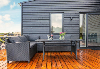 Udendørs terrasse med sort loungesæt, bord, vin og blomster ved 8 personers feriehus i Ansager, Danmark.