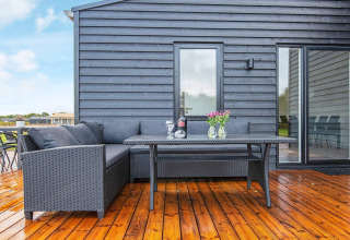 Terraza con conjunto lounge negro, mesa, vino y flores en casa vacacional para 8 personas en Ansager, Dinamarca.