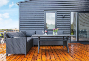 Terraza con conjunto lounge negro, mesa, vino y flores en casa vacacional para 8 personas en Ansager, Dinamarca.