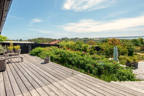 Terrasse en bois avec vue sur collines verdoyantes et mer au gîte 8 personnes d’Ebeltoft, Danemark.