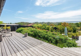 Terraza de madera con vistas a colinas verdes y el mar en la casa de vacaciones para 8 personas en Ebeltoft, Dinamarca.