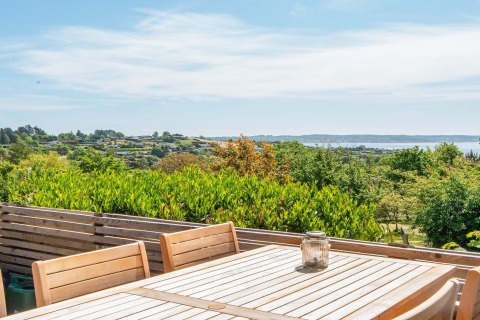 Vista dalla terrazza di legno con tavolo e sedie nella casa vacanza a Ebeltoft, Danimarca, su colline e mare.