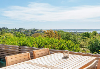 Vista dalla terrazza di legno con tavolo e sedie nella casa vacanza a Ebeltoft, Danimarca, su colline e mare.