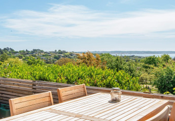 View from wooden terrace with table and chairs at 8 person holiday home in Ebeltoft, Denmark, overlooking hills and sea.