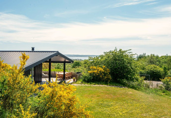 Moderne feriehytte i Ebeltoft med overdækket terrasse, grøn have og udsigt til havet, Danmark.