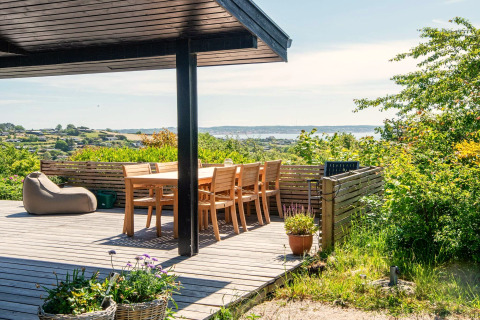 Terrasse ensoleillée du « gîte 8 personnes à Ebeltoft » au Danemark, vue sur la mer et le paysage verdoyant.