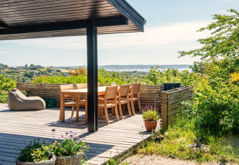 Solrig terrasse ved "8 personers feriehus i Ebeltoft" i Danmark med udsigt til havet og grønne omgivelser.