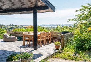 Zonnig terras bij "8 persoons vakantiehuis in Ebeltoft", Denemarken met uitzicht op zee en groene natuur.