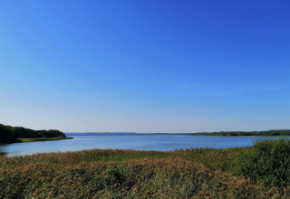 Zicht op het meer en de natuur vanuit het 8-persoons vakantiehuis in Ebeltoft, Denemarken, onder blauwe lucht.