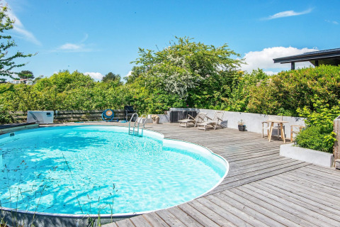 Outdoor swimming pool with wooden deck and sun loungers at 8 person holiday home in Ebeltoft, Denmark.