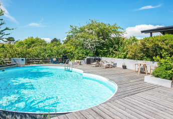 Outdoor swimming pool with wooden deck and sun loungers at 8 person holiday home in Ebeltoft, Denmark.
