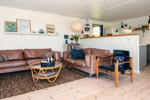 Salon d'une maison de vacances à Ebeltoft, au Danemark, avec canapés en cuir, table en rotin et déco claire.