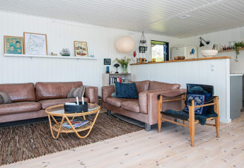 Living room in an Ebeltoft holiday home in Denmark with leather sofas, rattan table, and bright decor.
