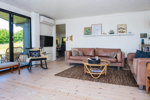 Lyst opholdsstue i sommerhus i Ebeltoft, Danmark, med moderne lædermøbler og store vinduer.