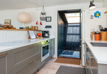 Modern kitchen in a holiday home in Ebeltoft, Denmark, featuring grey cabinets, a white countertop and open door.